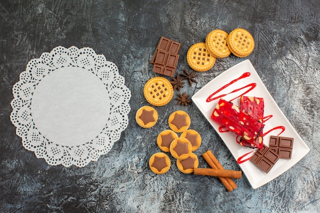 Phptp superior de un trozo de encaje blanco con galletas y un plato de chocolate surtido sobre fondo gris