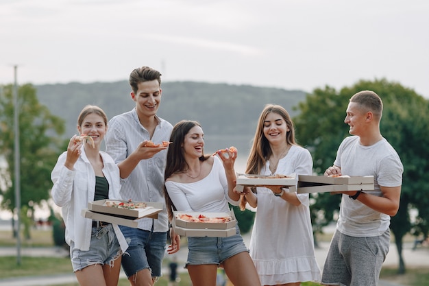 Picnic amigos con pizza y bebidas, día soleado, atardecer, compañía, diversión, parejas y mamá con bebé.