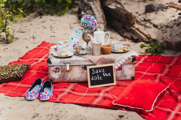 Picnic de naturaleza muerta romántico en una playa. Tazas, galletas, maleta en la cubierta roja