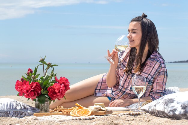 Un picnic romántico en la orilla arenosa de la playa con flores y vasos de bebida. El concepto de vacaciones de verano.