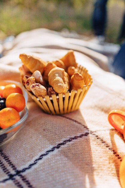 Picnic de verano en una alfombra con frutas, vino y té, tazas, croissants y detalles de dulces.