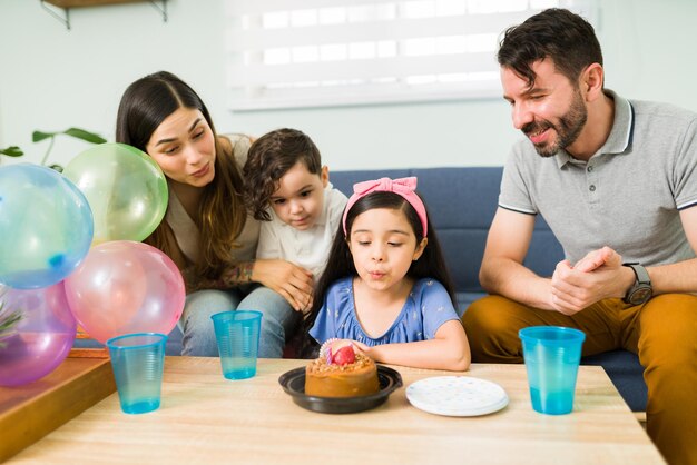 Pide un deseo. Hermosa niña soplando su vela de cumpleaños en un pastel mientras celebra con una fiesta en casa