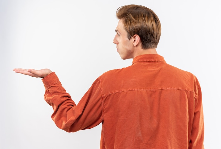 Foto gratuito de pie detrás de la vista chico guapo joven con camisa roja fingiendo sostener algo aislado en la pared blanca