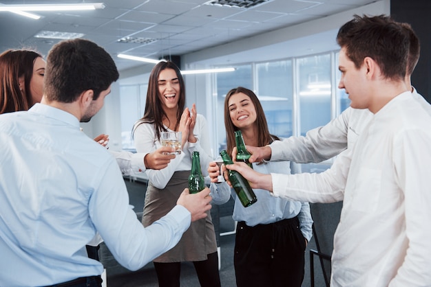 De pie y golpeando las botellas y el vaso. En la oficina. Los jóvenes celebran su éxito.