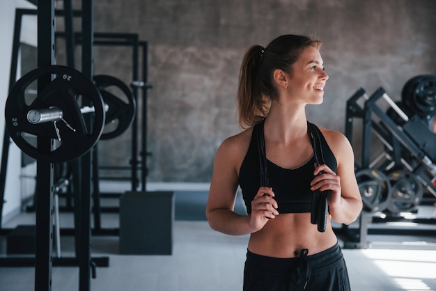 De pie con saltar la cuerda en las manos. Hermosa mujer rubia en el gimnasio en su fin de semana