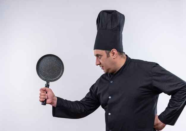 De pie en la vista de perfil, cocinero de sexo masculino de mediana edad en uniforme de chef sosteniendo una sartén puso su mano en la cadera con espacio de copia