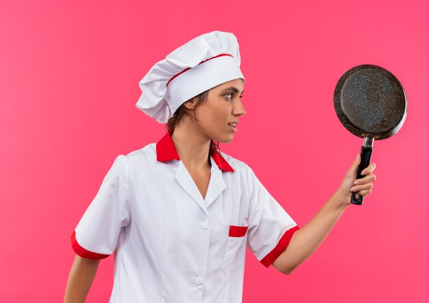 De pie en la vista de perfil joven cocinera vistiendo uniforme de chef sosteniendo una sartén con espacio de copia