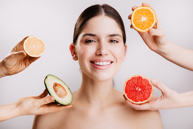 Piel radiante hermosa sana de mujer sin maquillaje. Retrato de niña sonriendo contra la pared de frutas.