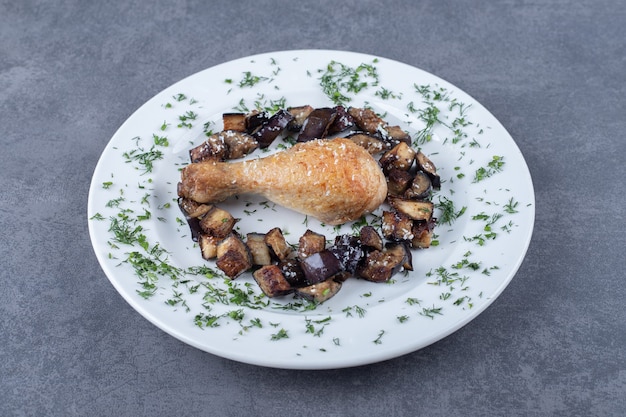 Pierna de pollo frito y berenjena en un plato blanco.