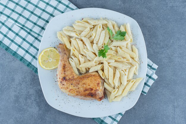 Pierna de pollo a la parrilla y pasta penne en un plato blanco.