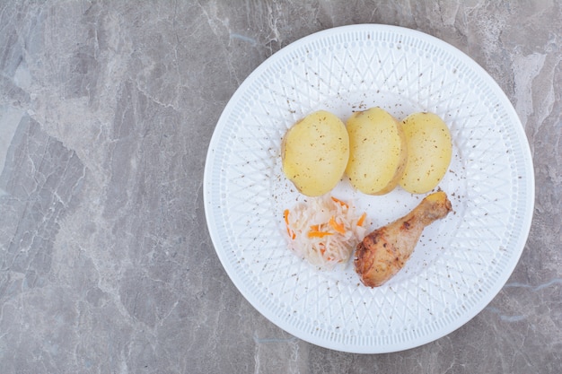 Pierna de pollo a la plancha, patatas y chucrut en un plato blanco.