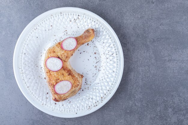 Pierna de pollo a la plancha y rábano en rodajas en un plato blanco.