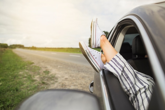 Las piernas de la mujer colgando de una ventana del coche estacionado en el borde de la carretera