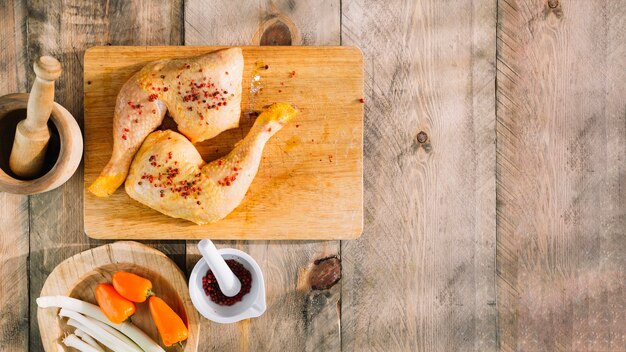 Piernas de pollo crudo en tablero de madera