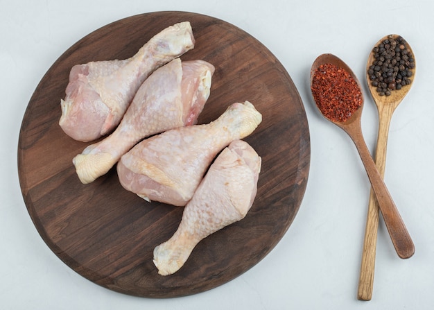 Piernas de pollo fresco crudo con dos pimientos de cuchara sobre fondo blanco.