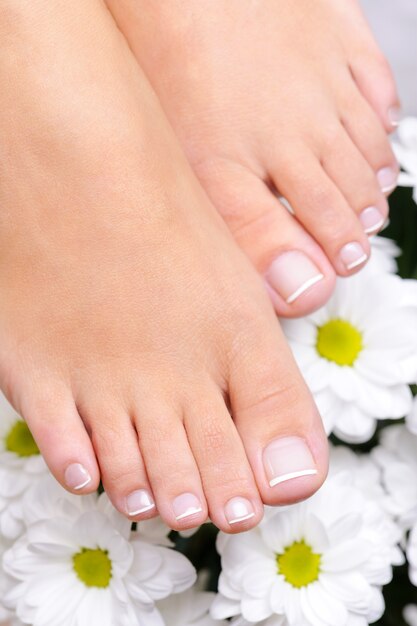 Pies femeninos bien cuidados con pedicura francesa y flores.