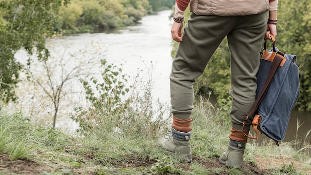 Los pies del hombre de pie sobre la hierba y sosteniendo la mochila