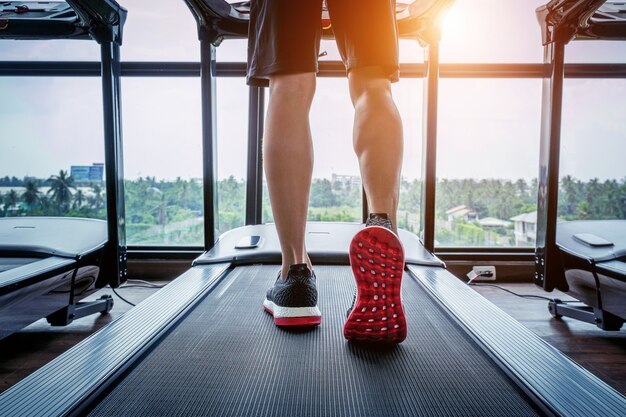 Pies masculinos en zapatillas corriendo en la cinta en el gimnasio. Concepto de ejercicio.