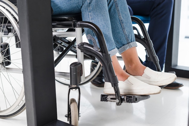 Pies de la mujer con discapacidad en silla de ruedas en piso blanco