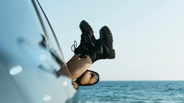 Pies de mujer fuera de la ventana del coche cerca del mar