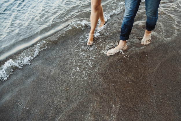 Pies de mujer y hombre van en la playa cerca del mar