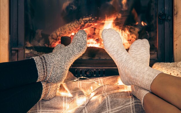 Los pies de las mujeres en calcetines cálidos se calientan junto a la chimenea de la casa