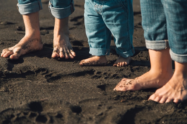 Pies de los padres y el bebé de pie en la playa de arena