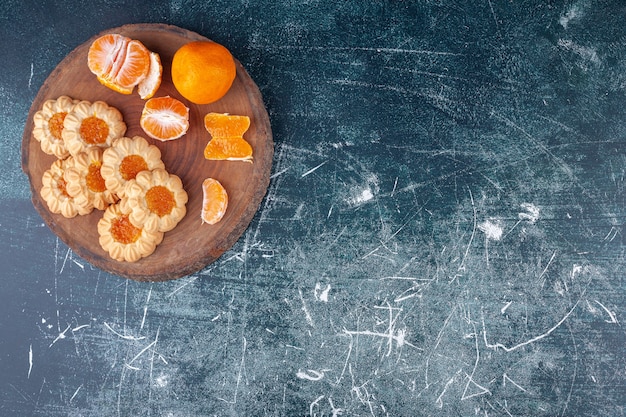 Pieza de madera con frutas de clementina y galletas de gelatina sobre fondo de mármol.