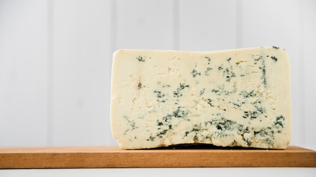 Pieza de queso azul en tabla de cortar de madera sobre escritorio blanco