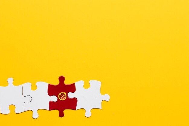 Pieza del rompecabezas rojo con el símbolo de la diana dispuesta con la pieza blanca sobre fondo amarillo