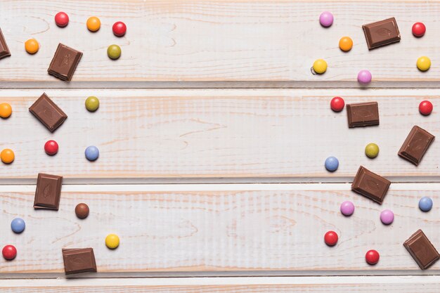 Piezas de chocolate y gemas de colores sobre fondo de madera con textura con espacio de copia para escribir el texto