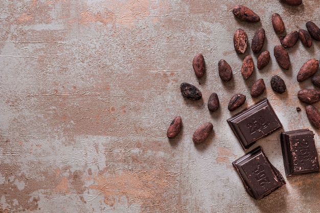 Piezas de chocolate con granos de cacao en bruto en el fondo rústico