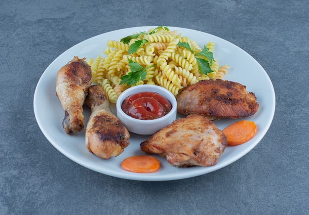 Piezas de pollo frito y fusilli en plato blanco.