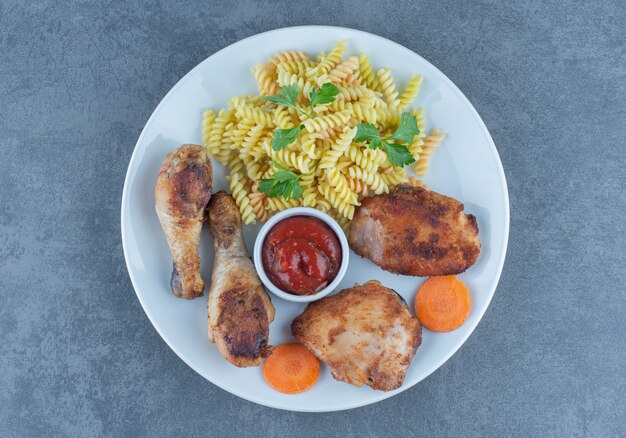 Piezas de pollo frito y fusilli en plato blanco.