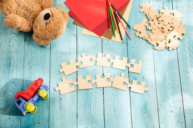 Piezas de rompecabezas, crayones, camión de juguete, osito de peluche y papel sobre una mesa de madera. Concepto de infancia y educación.