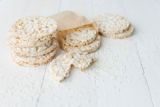 Pila de arroz inflado casero con granos derramados en mesa de madera blanca