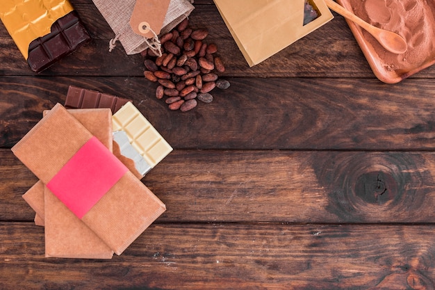 Pila de barras de chocolate, granos de cacao y polvo en el escritorio de madera
