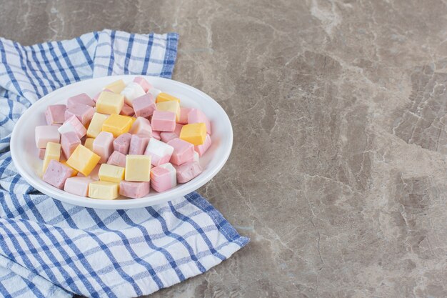 Pila de caramelos rosados y blancos en un plato blanco sobre fondo gris.