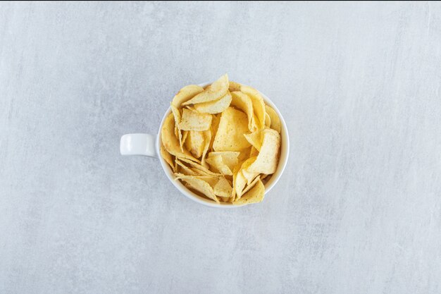 Pila de chips crujientes salados colocados en taza sobre piedra.