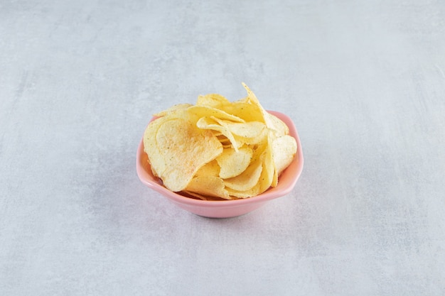 Pila de chips crujientes salados colocados en un tazón rosa sobre piedra.