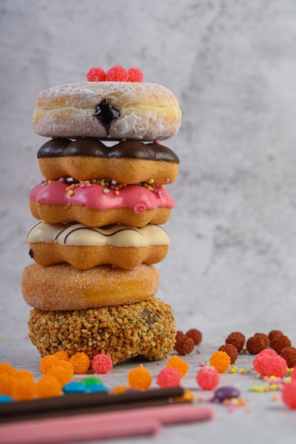 Pila de donuts surtidos y topping en un piso de cemento blanco.