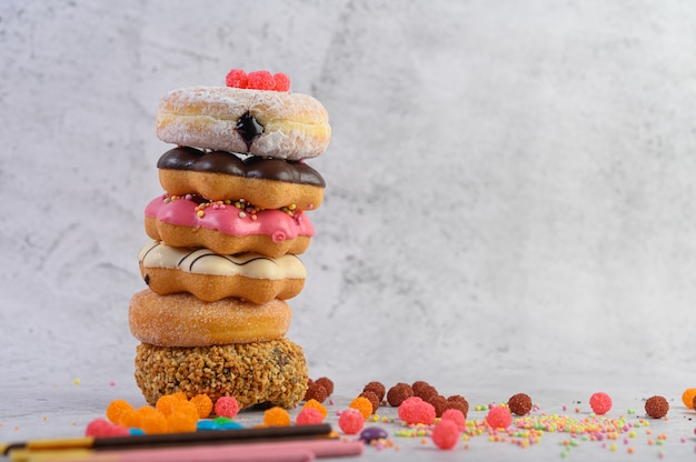 Pila de donuts surtidos y topping en un piso de cemento blanco.