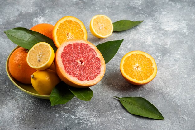 Pila de frutas cítricas en un tazón sobre mesa gris.