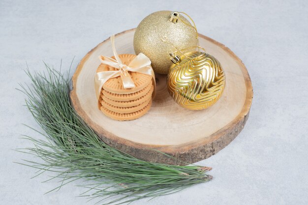 Pila de galletas atadas con cinta y bolas de Navidad sobre tabla de madera. Foto de alta calidad