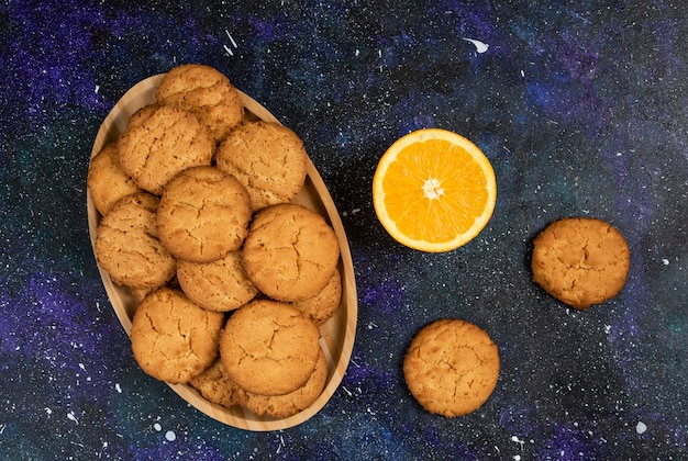 Pila de galletas caseras y media naranja cortada sobre una mesa oscura.