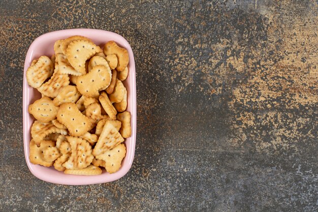 Pila de galletas saladas en un tazón rosa.