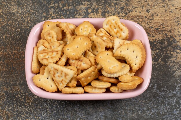 Pila de galletas saladas en un tazón rosa.