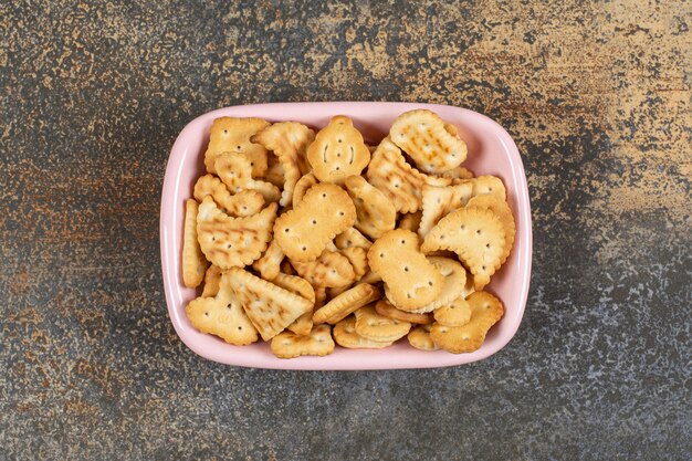 Pila de galletas saladas en un tazón rosa.