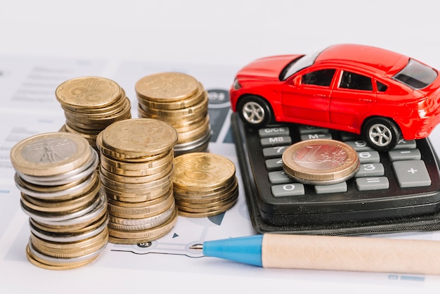 Foto gratuita pila de monedas; calculadora; coche de juguete y pluma en la plantilla