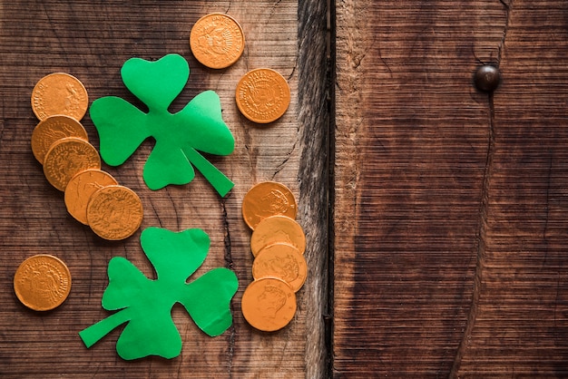 Pila de monedas y tréboles de papel verde en mesa de madera